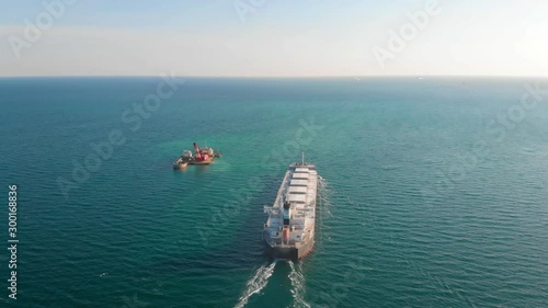 The large cargo vessel left the port after loading and moves in the right direction at high speed. Balker goes in the ocean.