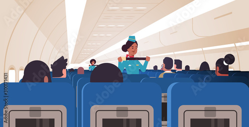 stewardess explaining passengers how to use seat belt fastening in emergency situation african american flight attendants in uniform safety demonstration concept airplane board interior horizontal