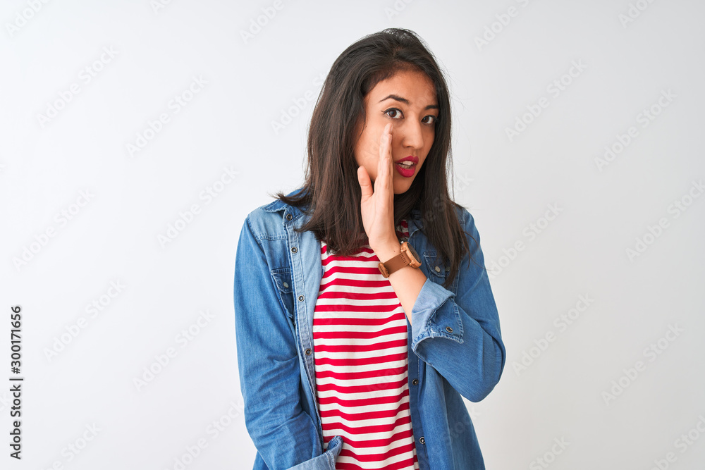 Young chinese woman wearing striped t-shirt and denim shirt over isolated white background hand on mouth telling secret rumor, whispering malicious talk conversation Young chinese woman wearing striped t-shirt and denim shirt over isolated white background hand on mouth telling secret rumor, whispering malicious talk conversation