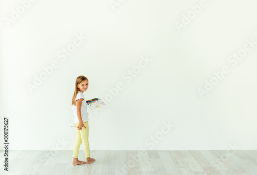 Little girl painting on white wall indoors