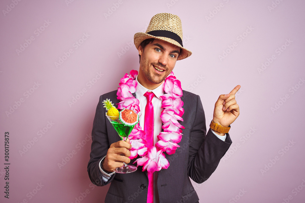 Businessman wearing suit hat hawaiian lei drinking cocktail over isolated pink background very happy pointing with hand and finger to the side Businessman wearing suit hat hawaiian lei drinking cocktail over isolated pink background very happy pointing with hand and finger to the side