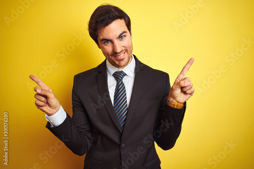 Young handsome businessman wearing suit and tie standing over isolated yellow background smiling confident pointing with fingers to different directions. Copy space for advertisement