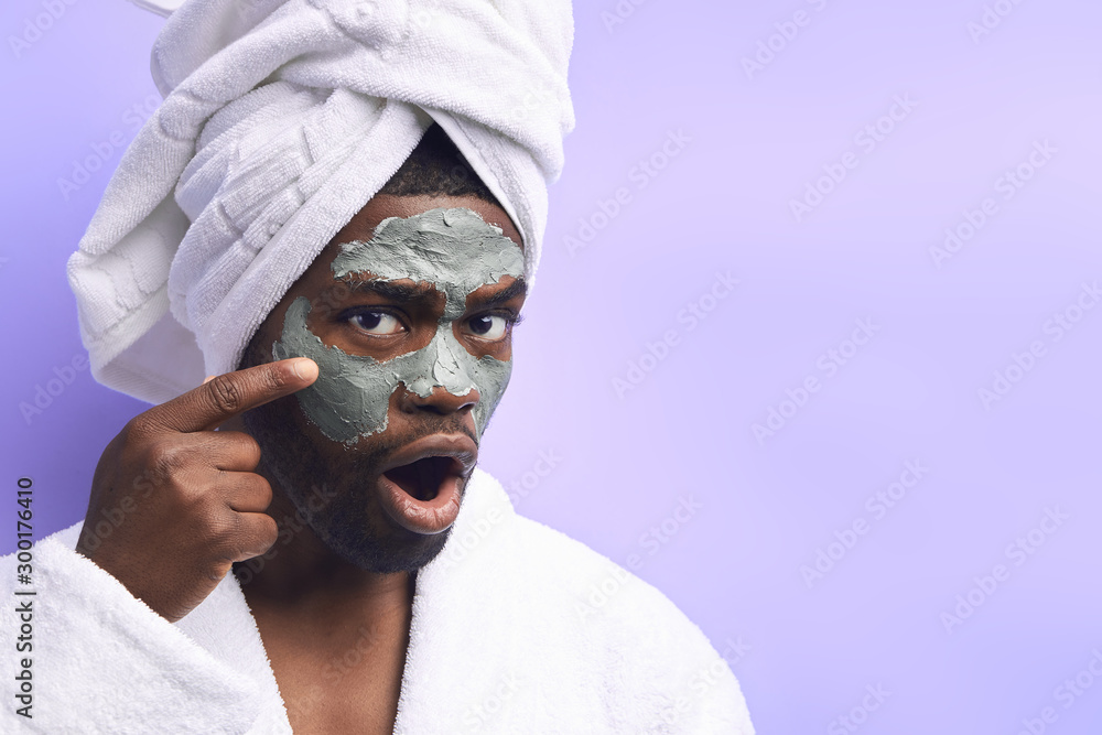 Emotional handsome man in towel and bathrobe wearing mask for face, look at camera Emotional handsome man in towel and bathrobe wearing mask for face, look at camera