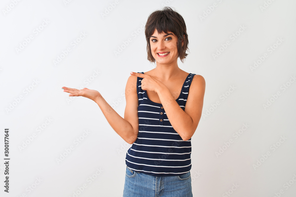 Young beautiful woman wearing striped t-shirt standing over isolated white background amazed and smiling to the camera while presenting with hand and pointing with finger. Young beautiful woman wearing striped t-shirt standing over isolated white background amazed and smiling to the camera while presenting with hand and pointing with finger.