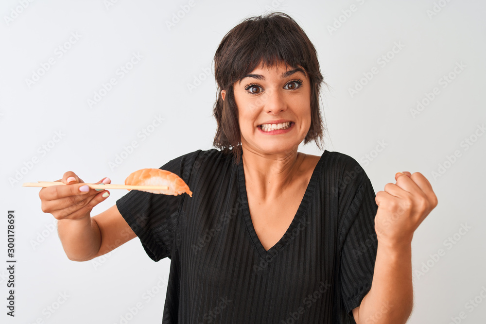 Obraz premium Beautiful woman eating salmon nigiri sushi using chopsticks over isolated white background screaming proud and celebrating victory and success very excited, cheering emotion