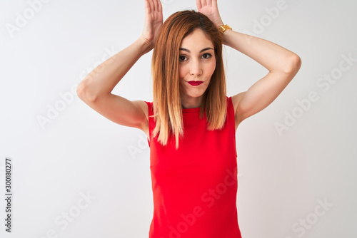 Redhead businesswoman wearing elegant red dress standing over isolated white background Doing bunny ears gesture with hands palms looking cynical and skeptical. Easter rabbit concept.