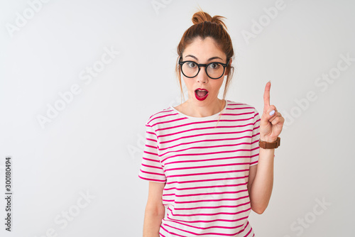 Redhead woman wearing glasses striped t-shirt and pigtail over isolated white background pointing finger up with successful idea. Exited and happy. Number one.