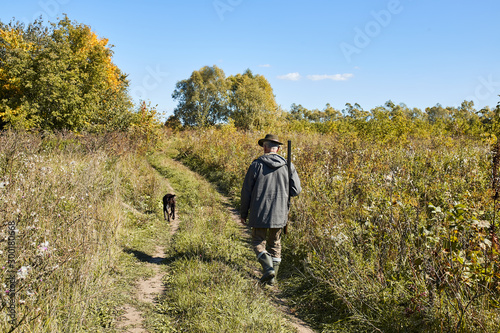 Photographie Rear view on hunter male with dog going to hunt in forest
