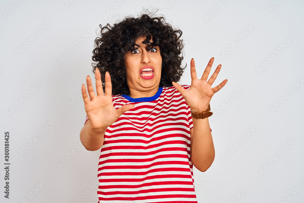 Young arab woman with curly hair wearing striped t-shirt over isolated white background afraid and terrified with fear expression stop gesture with hands, shouting in shock. Panic concept. Young arab woman with curly hair wearing striped t-shirt over isolated white background afraid and terrified with fear expression stop gesture with hands, shouting in shock. Panic concept.