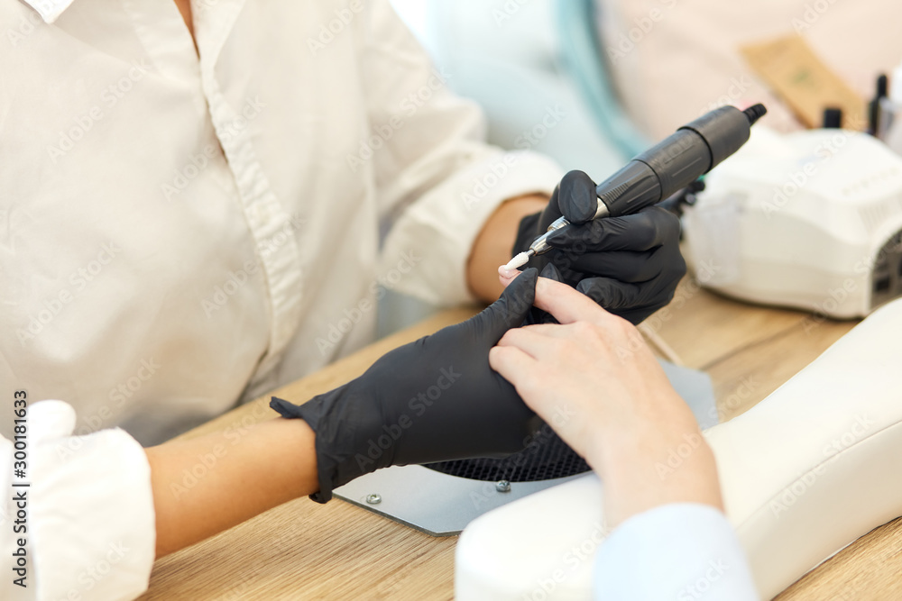 Manicurist in black gloves do mechanical manicure of nails. Closeup of beautiful hands. clean and sterile