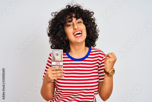Young arab woman with curly hair holding dollars standing over isolated white background screaming proud and celebrating victory and success very excited, cheering emotion