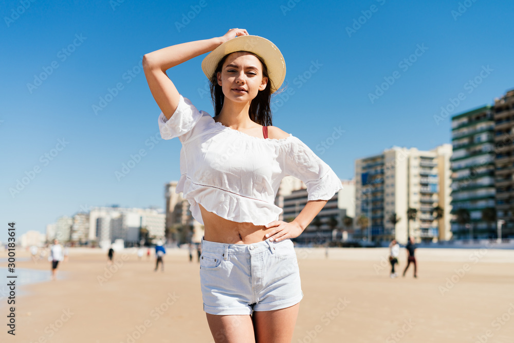 tourist in a hat and shorts posing on the beach on the background of houses tourist in a hat and shorts posing on the beach on the background of houses