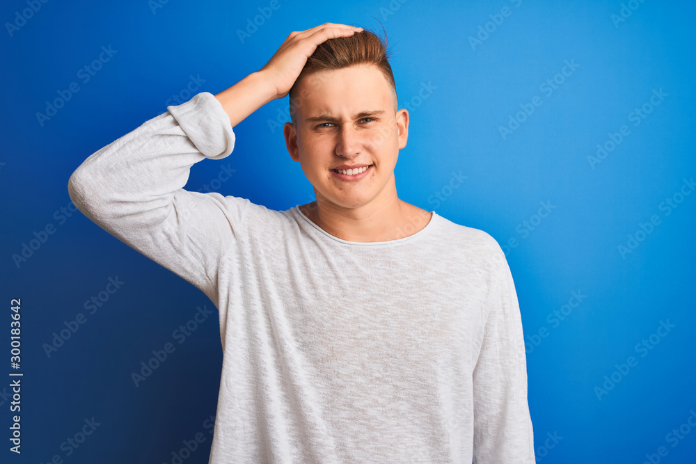 Young handsome man wearing white casual t-shirt standing over isolated blue background stressed with hand on head, shocked with shame and surprise face, angry and frustrated. Fear and upset Young handsome man wearing white casual t-shirt standing over isolated blue background stressed with hand on head, shocked with shame and surprise face, angry and frustrated. Fear and upset