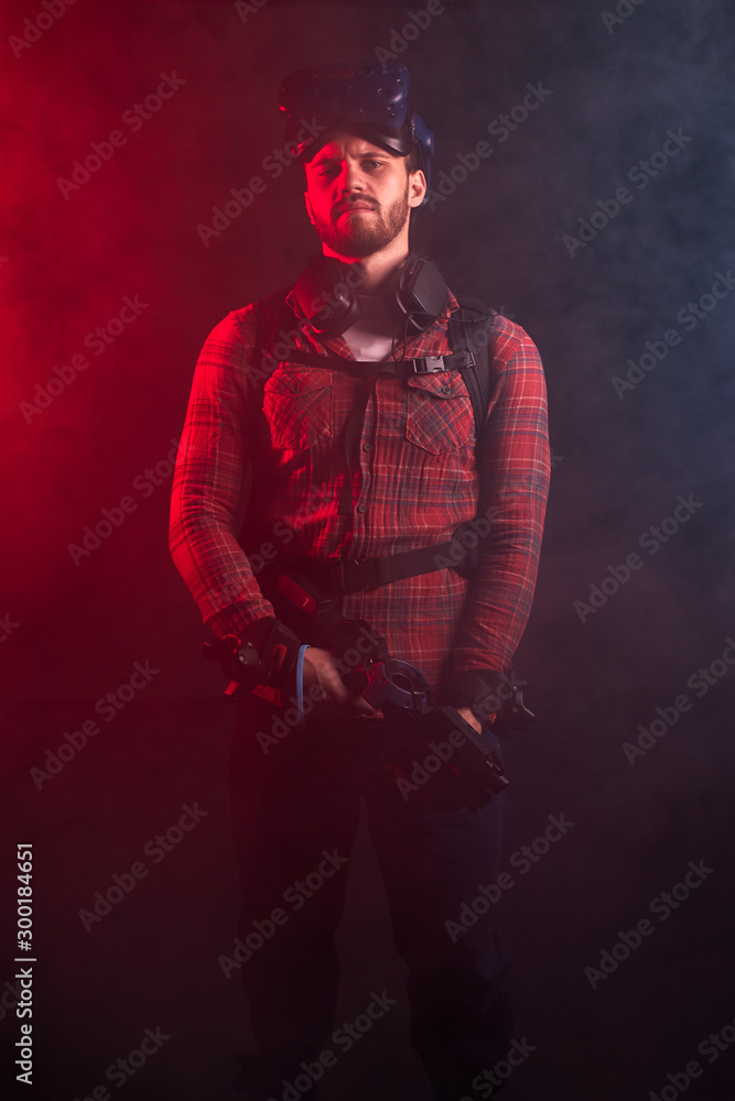 Portrait of young caucasian man looking at camera, holding virtual reality gun, special mask on head. Portrait of young caucasian man looking at camera, holding virtual reality gun, special mask on head.