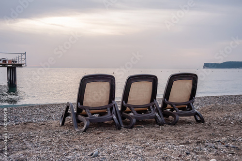 Three sun loungers stand on the beach by the sea © Vitaliy