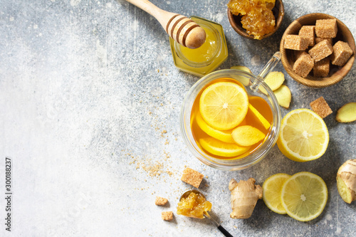 Hot cup of ginger tea and ingredients - lemon, ginger, honeycomb, honey on a gray stone countertop. Top view flat lay. Free space for your text.