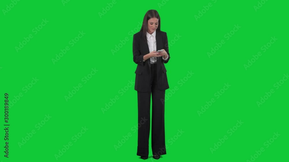Cheerful excited young business woman in suit reading message on mobile phone. Full length on green screen background. Cheerful excited young business woman in suit reading message on mobile phone. Full length on green screen background.