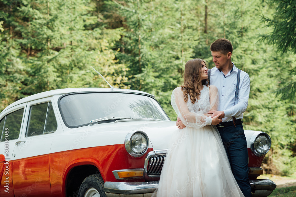 Fototapeta premium Happy luxury wedding couple kissing and embracing near retro car.