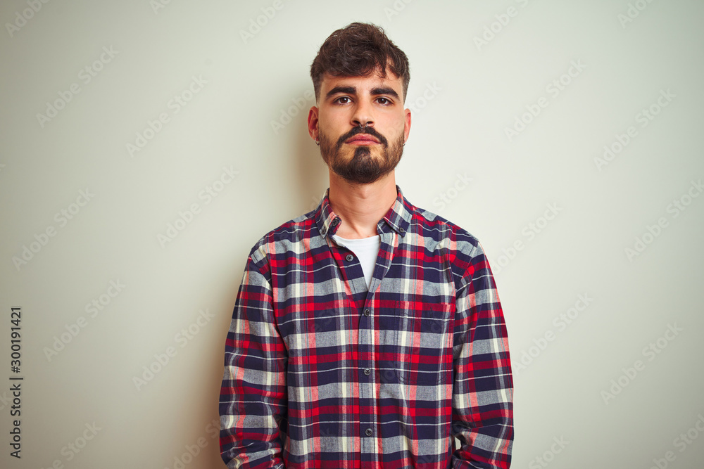 Obraz premium Young man wearing casual shirt standing over isolated white background with serious expression on face. Simple and natural looking at the camera.