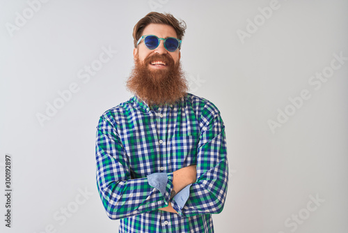 Young redhead irish man wearing casual shirt and sunglasses over isolated white background happy face smiling with crossed arms looking at the camera. Positive person.