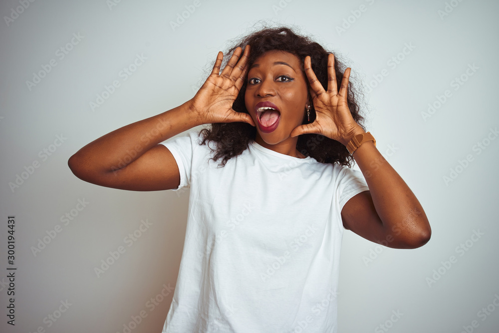 Young african american woman wearing t-shirt standing over isolated white background Smiling cheerful playing peek a boo with hands showing face. Surprised and exited Young african american woman wearing t-shirt standing over isolated white background Smiling cheerful playing peek a boo with hands showing face. Surprised and exited