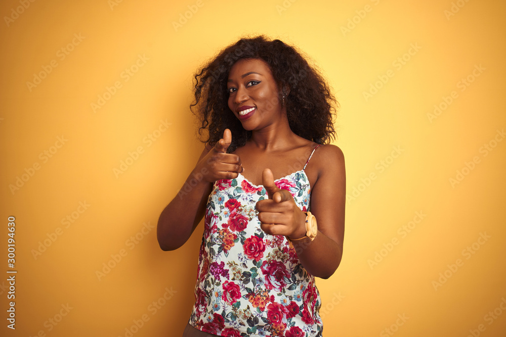 African american woman wearing floral summer t-shirt over isolated yellow background pointing fingers to camera with happy and funny face. Good energy and vibes.