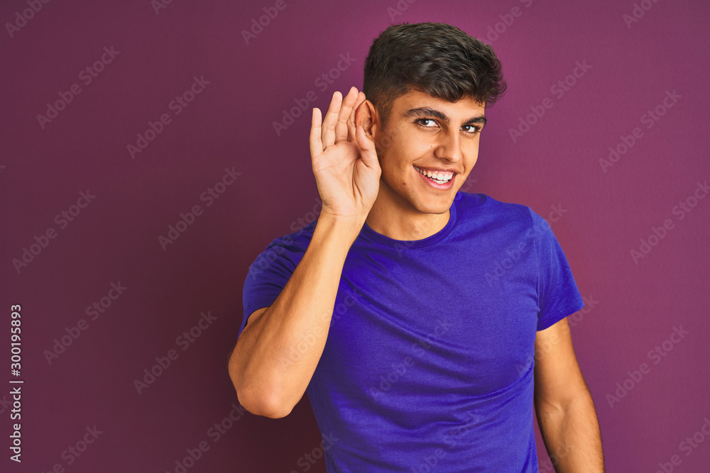 Young indian man wearing t-shirt standing over isolated purple background smiling with hand over ear listening an hearing to rumor or gossip. Deafness concept. Young indian man wearing t-shirt standing over isolated purple background smiling with hand over ear listening an hearing to rumor or gossip. Deafness concept.
