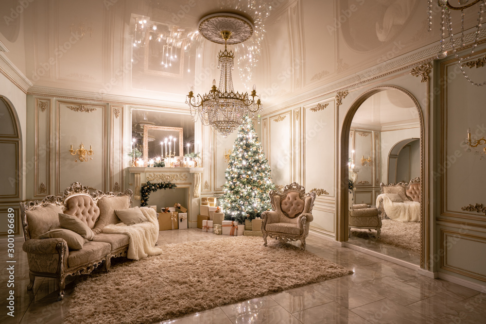 Christmas evening in the light of candles and garlands. Classic luxurious apartments with decorated christmas tree and presents. Living with fireplace, columns and stucco. - obrazy, fototapety, plakaty 