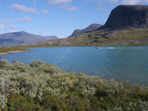 Wallpaper Mural Lapland nature landscape with blue glacial lake Alesjaure with motor boat, birch tree forest, snow capped mountains. Northern Sweden, at Kungsleden hiking trail. Summer sunny day Torontodigital.ca
