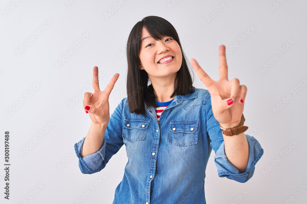 Young beautiful chinese woman wearing denim shirt over isolated white background smiling looking to the camera showing fingers doing victory sign. Number two. Young beautiful chinese woman wearing denim shirt over isolated white background smiling looking to the camera showing fingers doing victory sign. Number two.