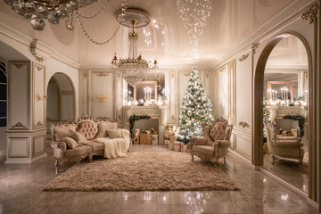 Christmas evening in the light of candles and garlands. Classic luxurious apartments with decorated christmas tree and presents. Living with fireplace, columns and stucco.