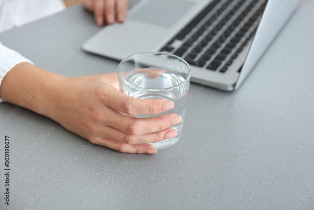 Woman with glass of fresh water and laptop working in office, closeup