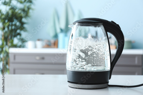 Transparent electric kettle with boiling water on table in kitchen photo