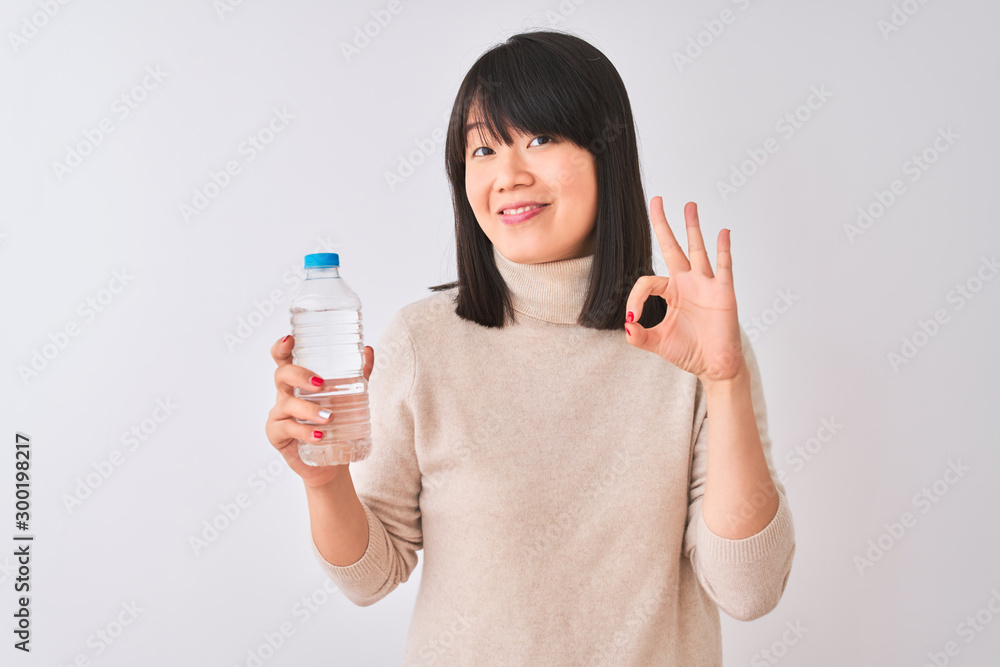 Young beautiful Chinese woman holding bottle of water over isolated white background doing ok sign with fingers, excellent symbol Young beautiful Chinese woman holding bottle of water over isolated white background doing ok sign with fingers, excellent symbol