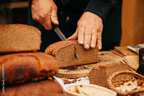 hands with bread man is cutting dark bread with knife