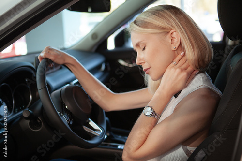 Beautiful blond haired woman rubbing her aching neck, sitting in her car. Female driver rubbing her neck, tired from driving © mad_production