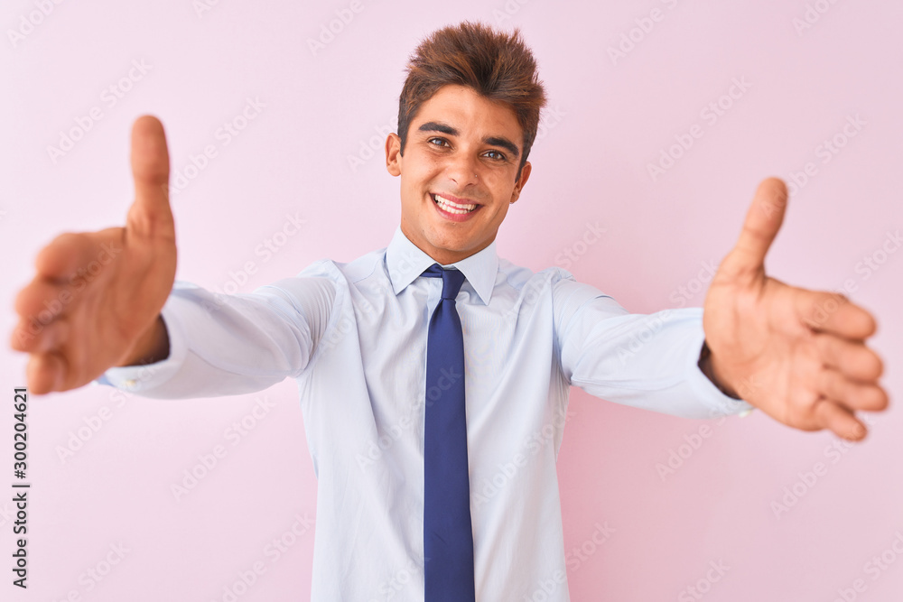Young handsome businessman wearing shirt and tie standing over isolated pink background looking at the camera smiling with open arms for hug. Cheerful expression embracing happiness. Young handsome businessman wearing shirt and tie standing over isolated pink background looking at the camera smiling with open arms for hug. Cheerful expression embracing happiness.