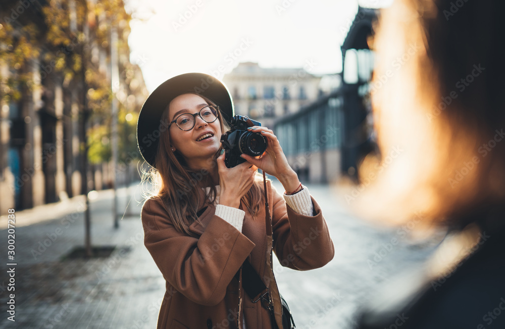 Photographer with retro camera take photo model girlfriend. Tourist smile girl in hat travels in Barcelona holiday with traveler friend. Sunlight flare street in europe. Photoshoot concept in city.