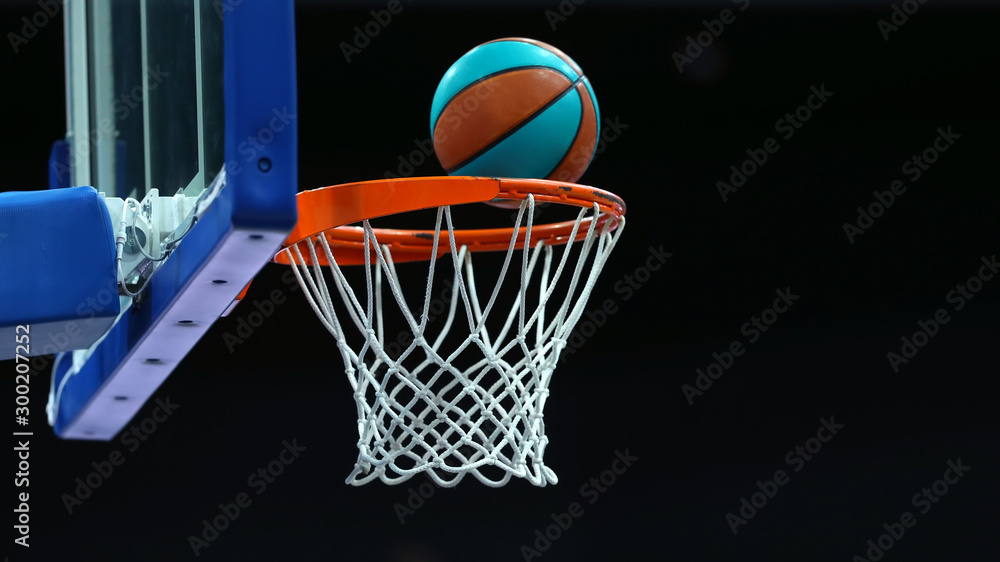 Basketball ring with a net in which the ball flies on a dark background in a sports complex