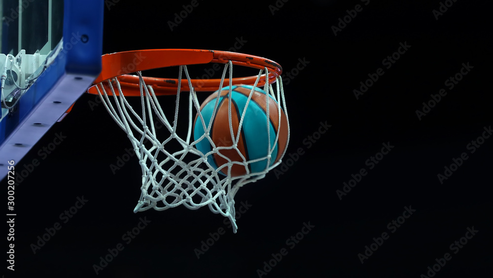 Fototapeta Basketball ring with a net in which the ball flies on a dark background in a sports complex