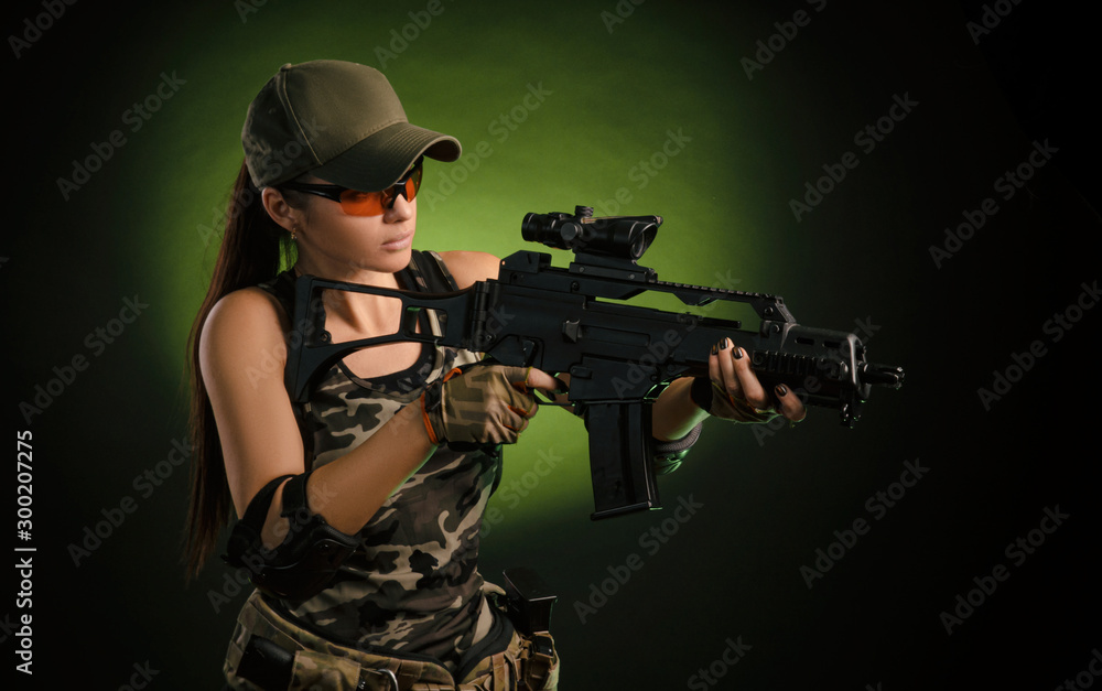the girl in military overalls airsoft posing with a gun in his hands on a dark background in the haze
