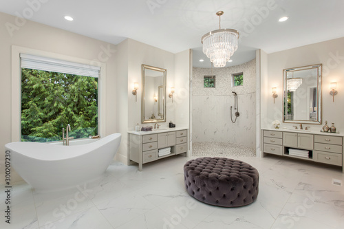 Elegant master bathroom in new luxury home, with two vanities, walk-in shower, soaking tub, and chandelier photo