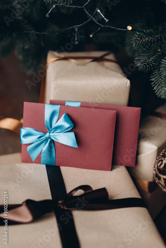 Gift voucher in burgundy envelope with blue bow under the Christmas tree. Christmas gift