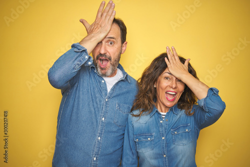 Canvastavla Beautiful middle age couple together standing over isolated yellow background surprised with hand on head for mistake, remember error