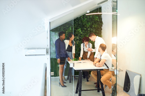 Successful young business team gathered in isolated modern office with glass wall, green background