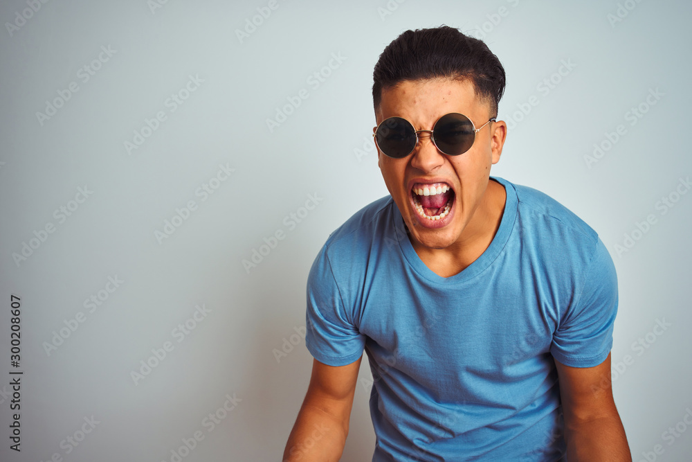 Young brazilian man wearing blue t-shirt and sunglasses over isolated white background very happy and excited doing winner gesture with arms raised, smiling and screaming for success Young brazilian man wearing blue t-shirt and sunglasses over isolated white background very happy and excited doing winner gesture with arms raised, smiling and screaming for success