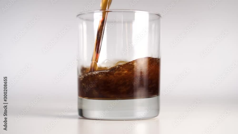 A bubbling dark cola pours and fills a glass beaker on a white background. Beautiful curly flows with bubbles. Slow motion A bubbling dark cola pours and fills a glass beaker on a white background. Beautiful curly flows with bubbles. Slow motion
