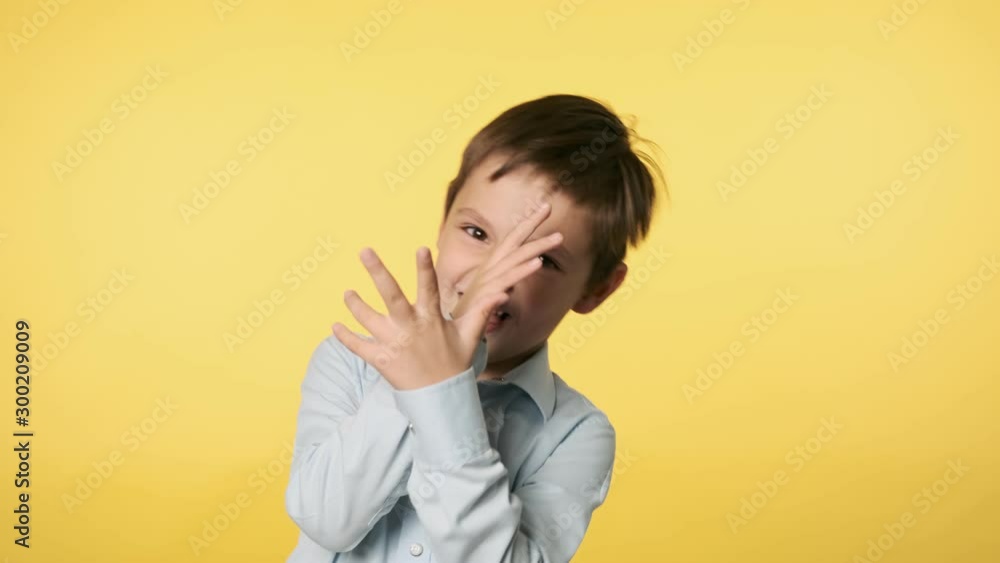 Portrait of cute little boy playfully making faces looking at camera. Caucasian kid boy in blue shirt doing silly funny face at yellow background. Positive emotion. Medium shot in 4k, UHD Portrait of cute little boy playfully making faces looking at camera. Caucasian kid boy in blue shirt doing silly funny face at yellow background. Positive emotion. Medium shot in 4k, UHD