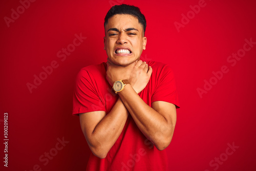 Young brazilian man wearing t-shirt standing over isolated red background shouting suffocate because painful strangle. Health problem. Asphyxiate and suicide concept.