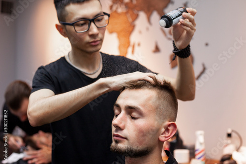 young barber kazakh works in a barbershop, handsome guy does hair styling for a client with dry gel in a hairdresser